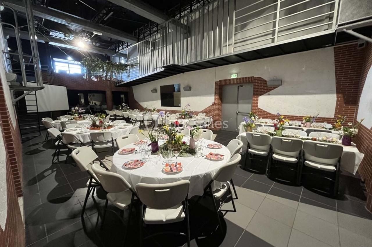 Salle de réception avec tables rondes dressées, nappes blanches, chaises pliantes et décoration florale.
