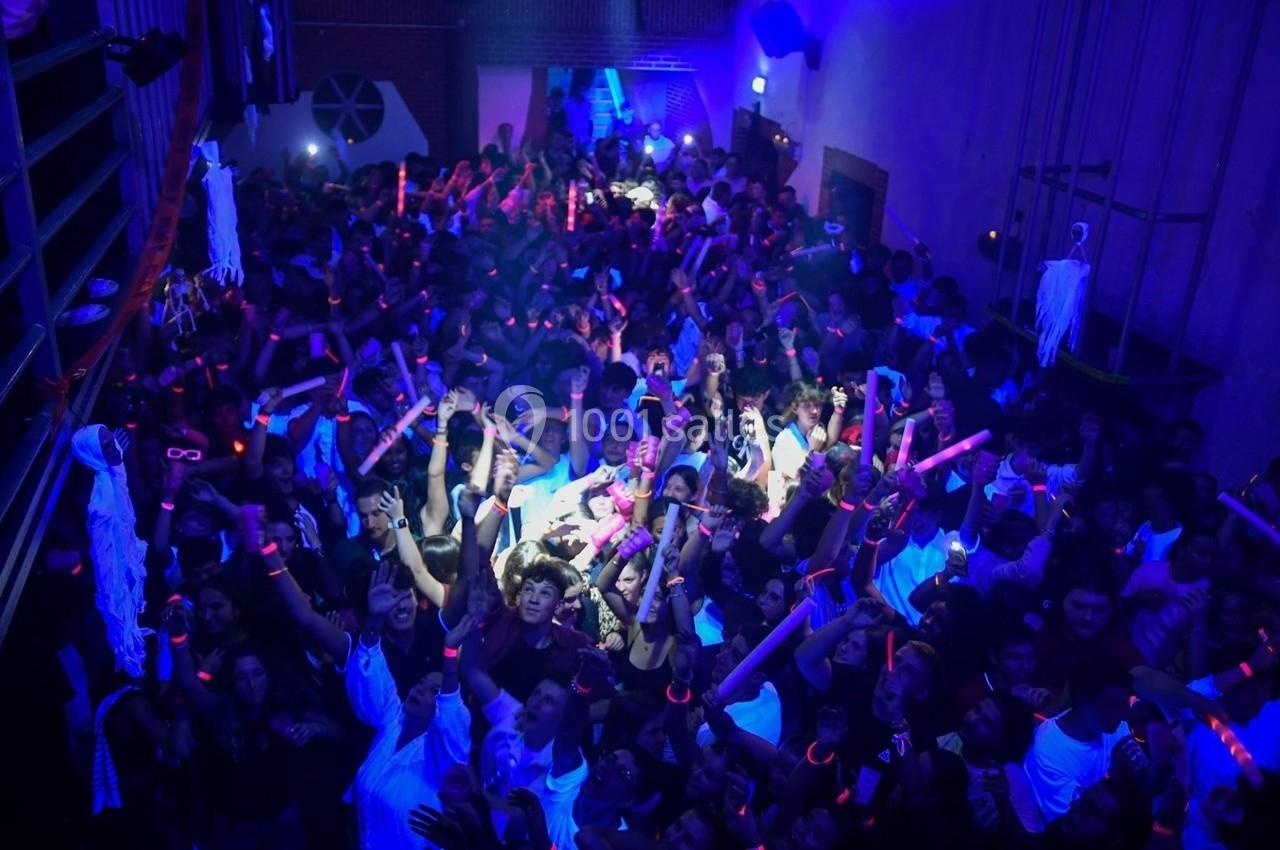 Foule dans une discothèque sombre avec des lumières bleues et des bâtons lumineux roses.