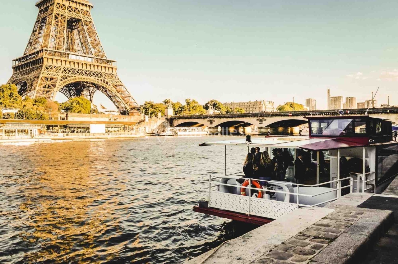 Bateau de tourisme amarré sur la Seine avec la tour Eiffel et un pont en arrière-plan par temps ensoleillé.