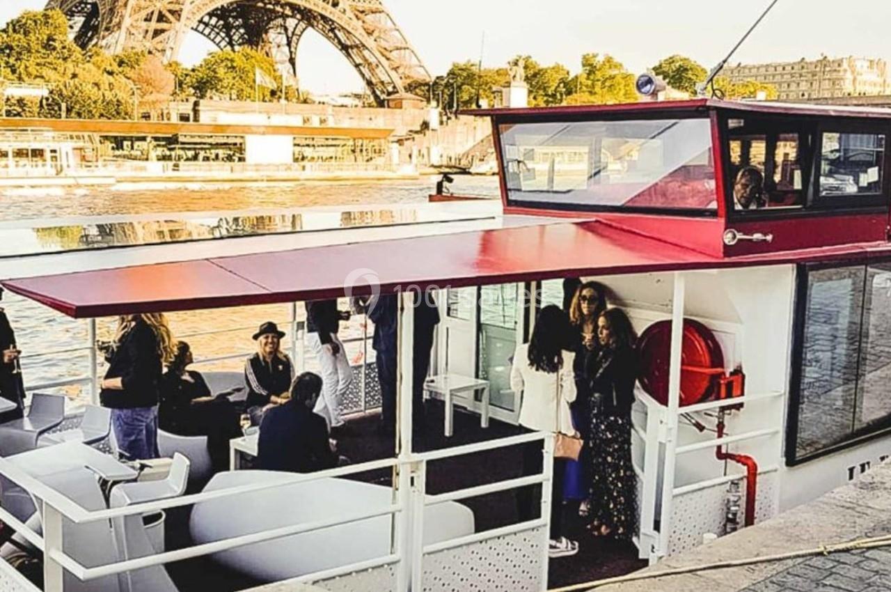 Bateau amarré sur la Seine avec des passagers à bord, la tour Eiffel visible en arrière-plan.