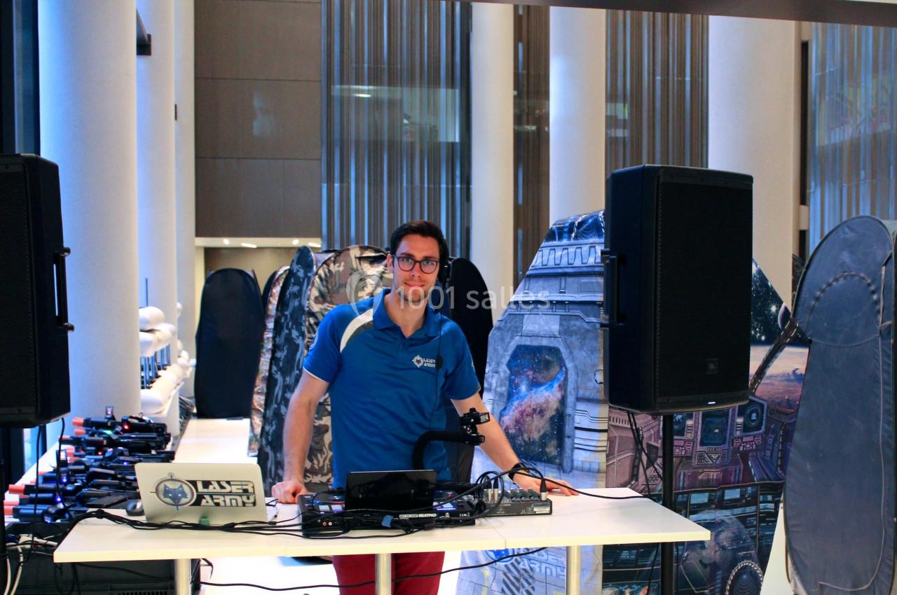 Un homme debout derrière une table équipée de matériel audio, dans un espace intérieur avec des décors futuristes.