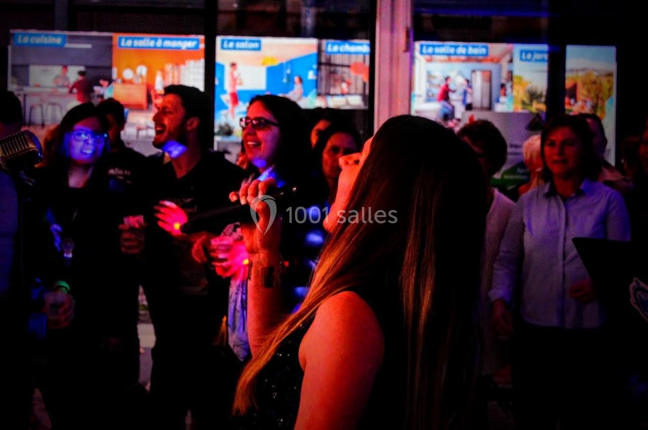 Une femme chante au micro devant un groupe de personnes dans un environnement lumineux et festif.