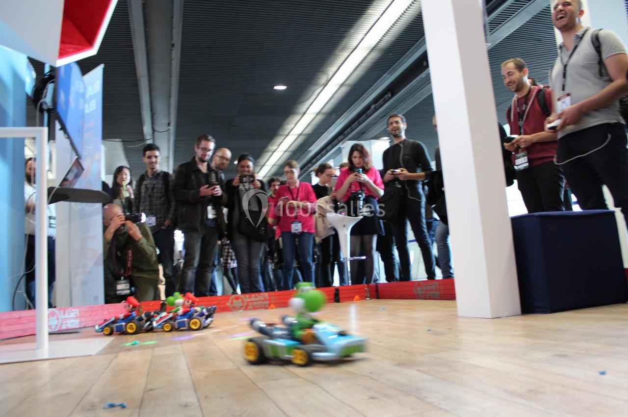 Des personnes observent et contrôlent des petites voitures télécommandées sur une piste intérieure en bois.