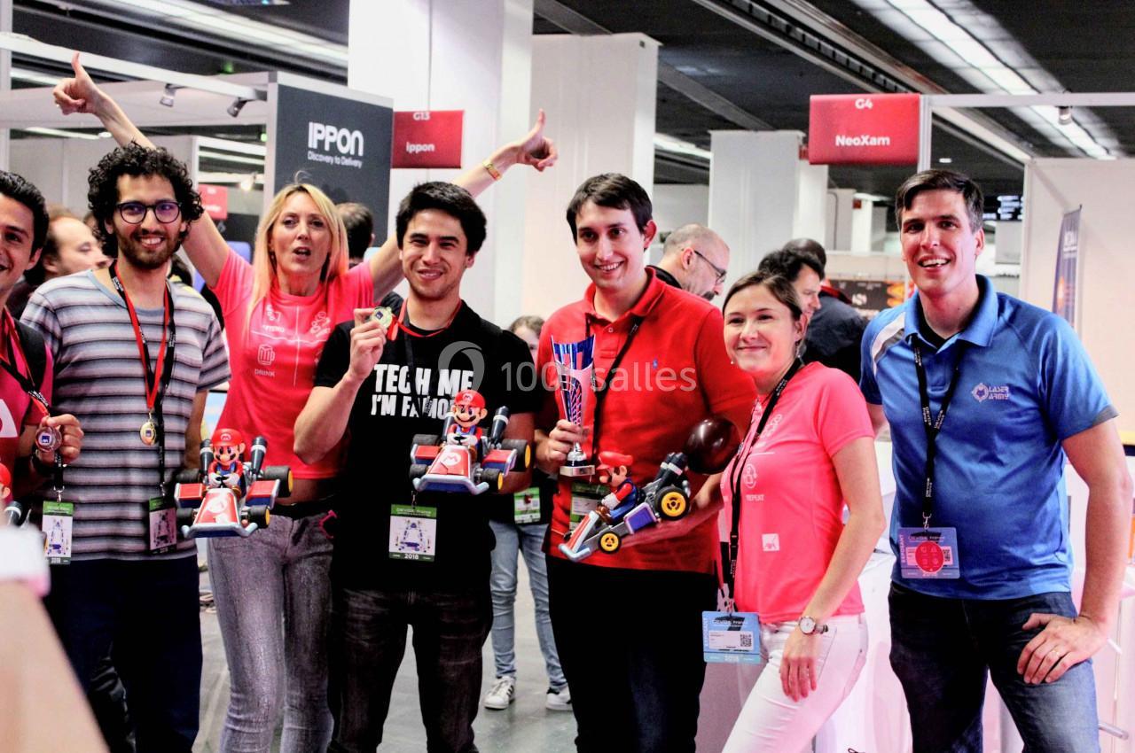 Un groupe de personnes souriantes posant avec des trophées et des objets colorés dans un espace d'exposition.