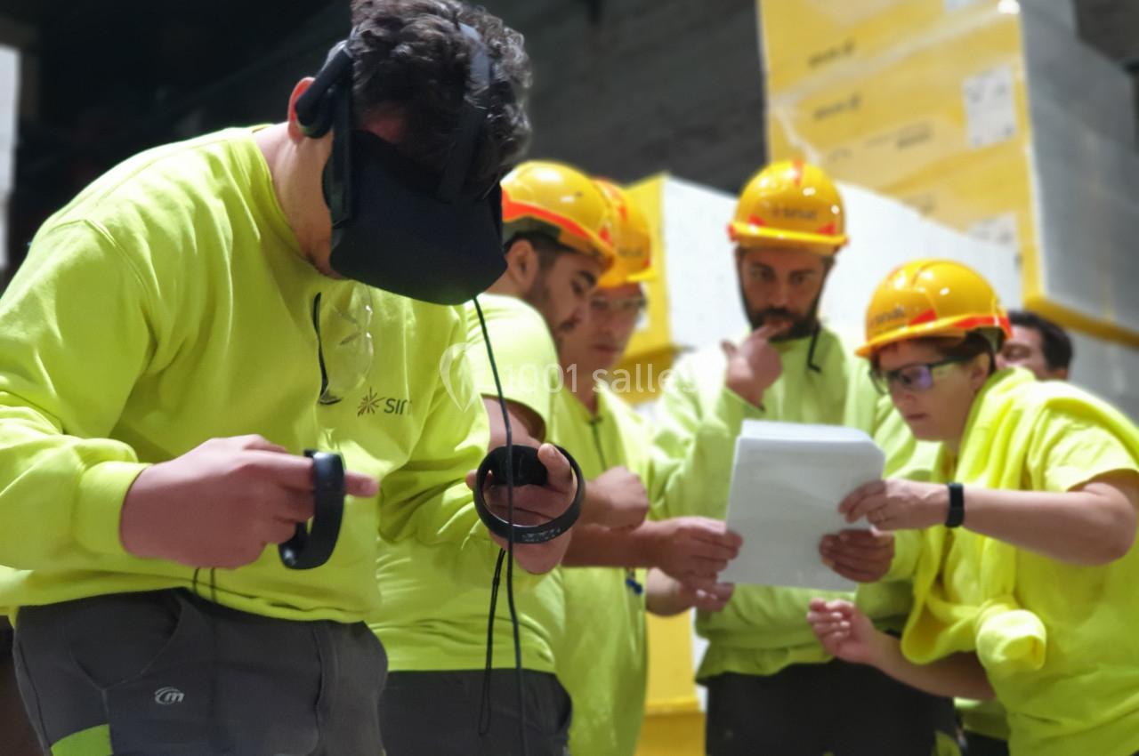 Des ouvriers en tenue de sécurité utilisent un casque de réalité virtuelle et consultent des documents dans un entrepôt.