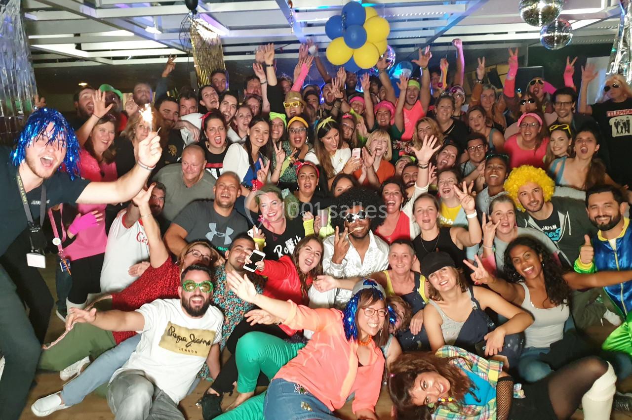 Groupe de personnes souriantes posant lors d'une fête costumée dans une salle décorée avec des ballons et des guirlandes.