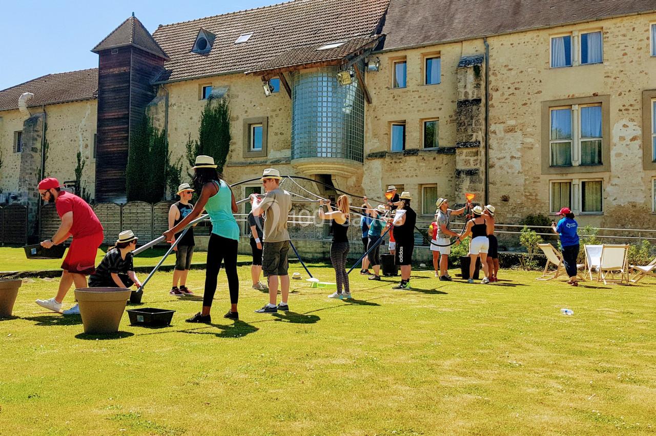 Un groupe de personnes participe à une activité en plein air sur une pelouse devant un bâtiment en pierre.