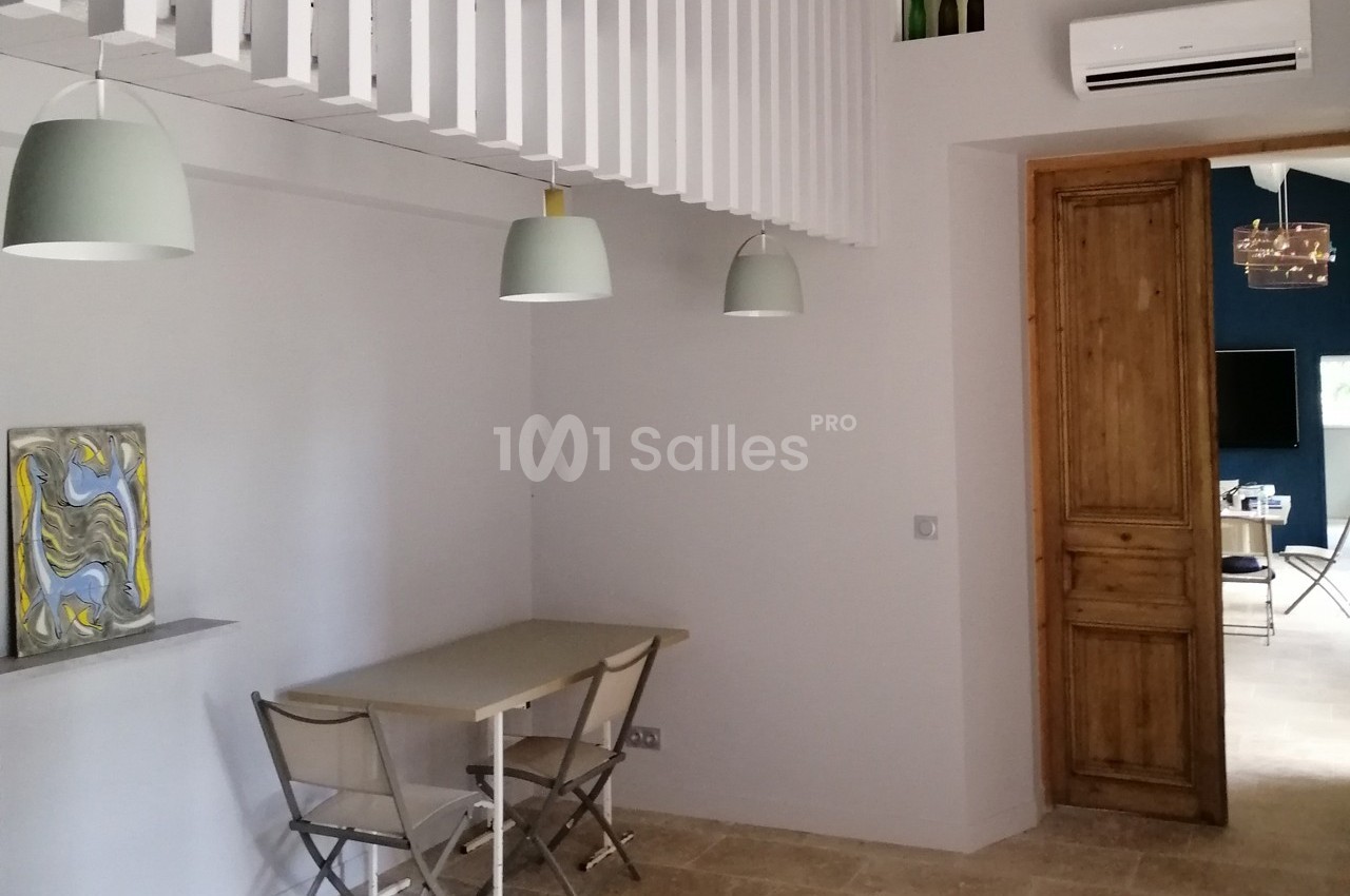 Salle à manger lumineuse avec table, chaises pliantes, suspensions modernes et porte en bois.