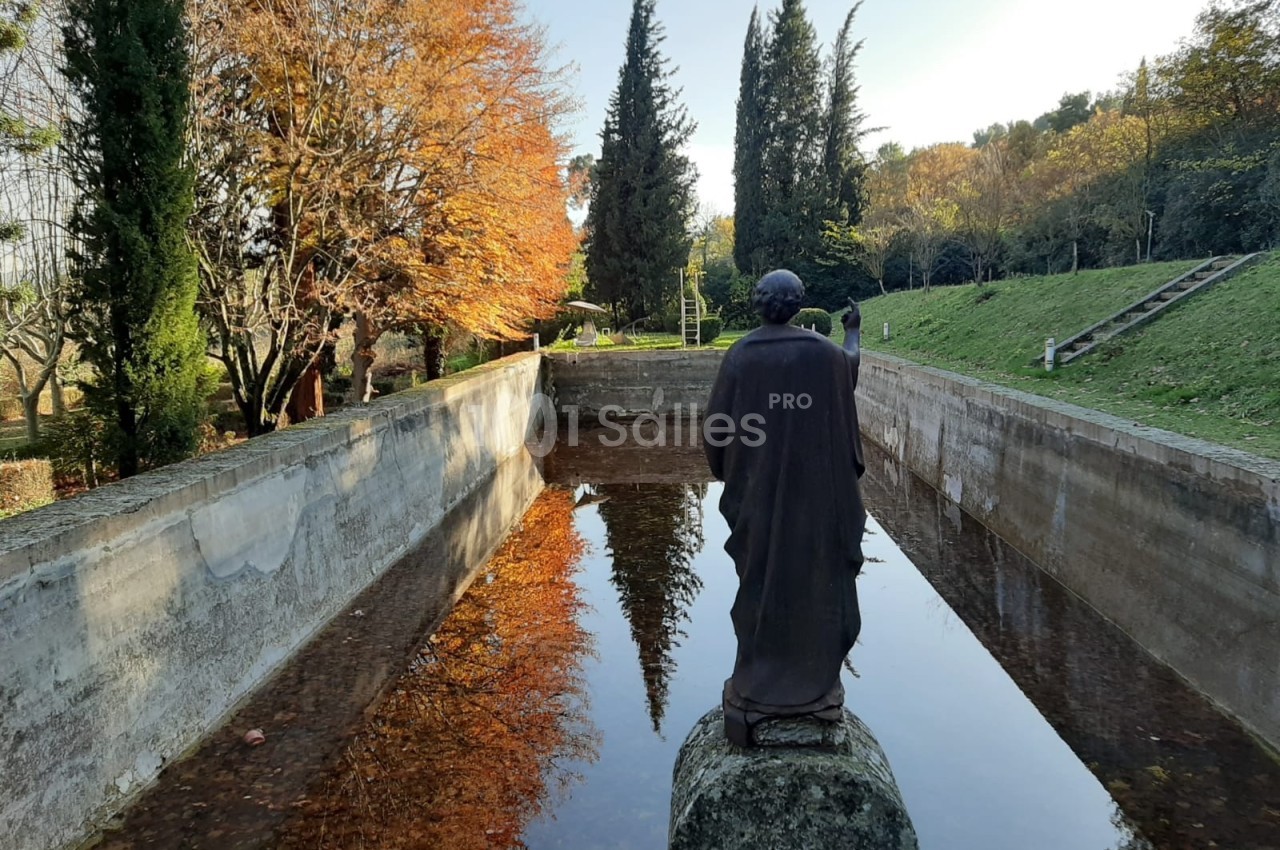 Statue de dos devant un bassin rectangulaire entouré d'arbres aux couleurs automnales.