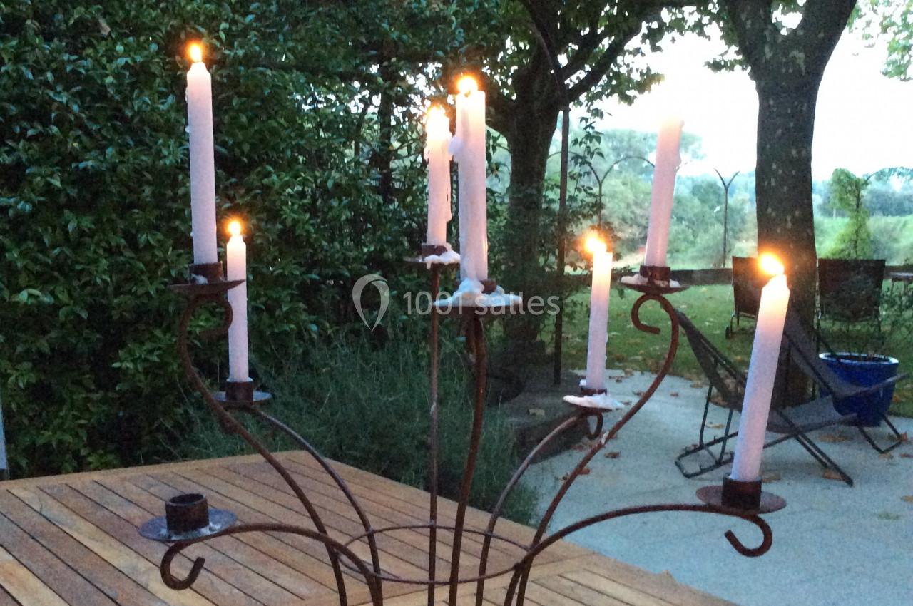 Chandelier en métal avec bougies allumées, posé sur une table en bois dans un jardin au crépuscule.