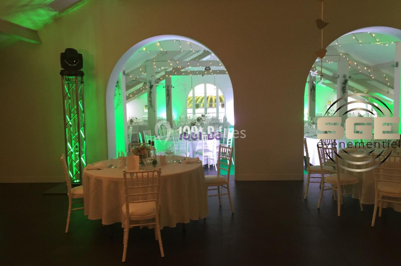 Salle de réception décorée avec des tables rondes, des chaises blanches et un éclairage vert diffus.