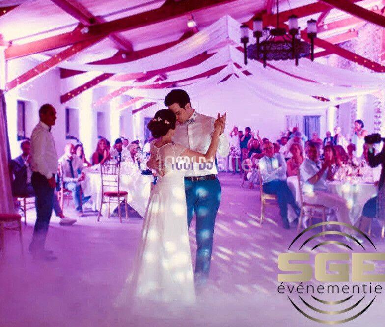 Un couple danse au centre d'une salle décorée pour un mariage, entouré d'invités assis à des tables.