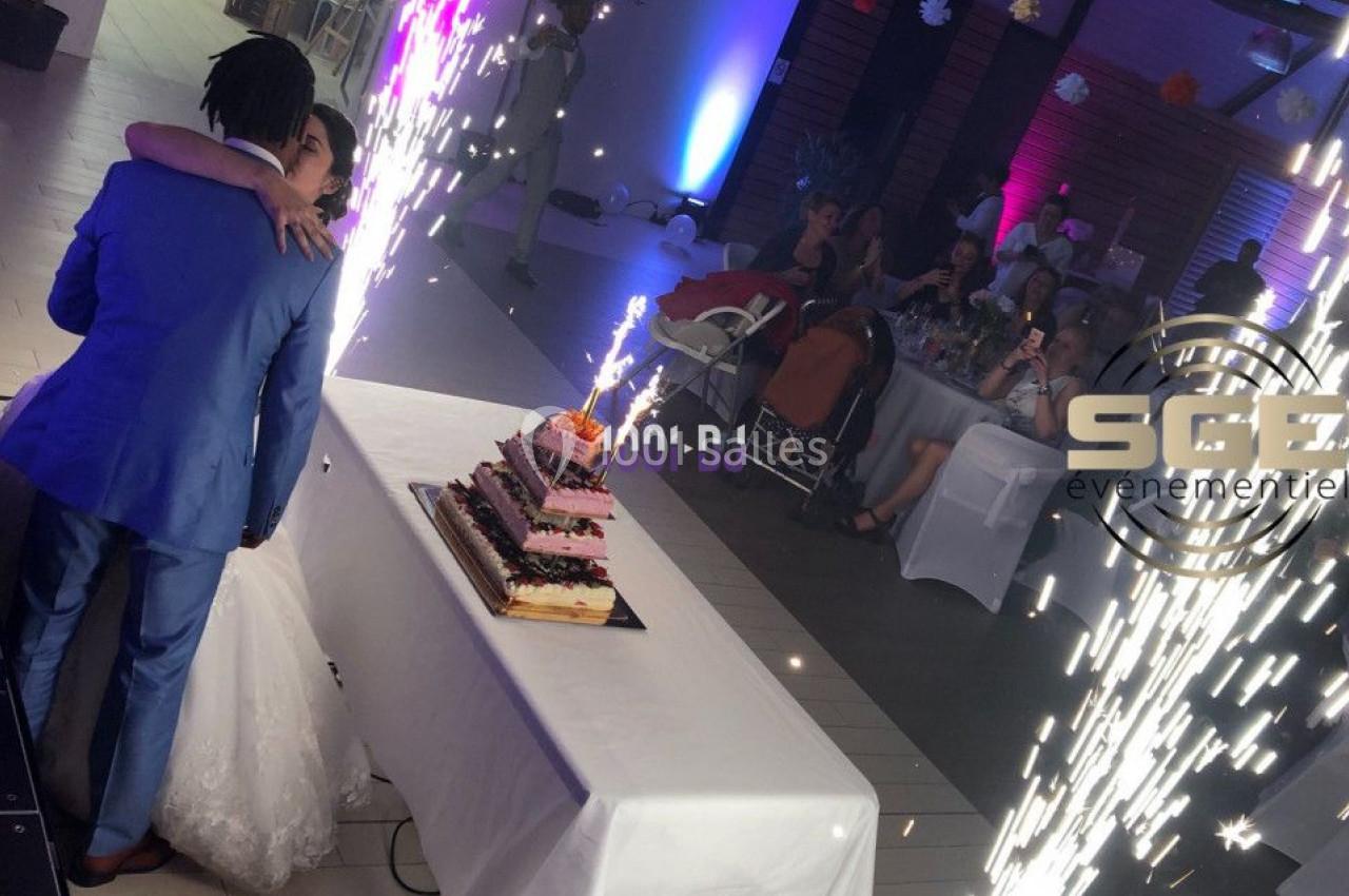 Un couple de mariés s'embrasse devant une table avec un gâteau et des fontaines d'étincelles allumées.