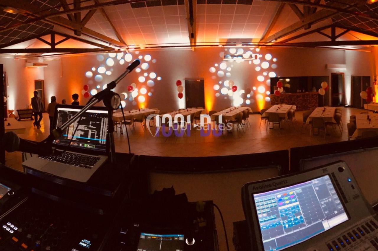 Salle de réception décorée avec des lumières colorées, vue depuis une table de mixage avec des équipements DJ.