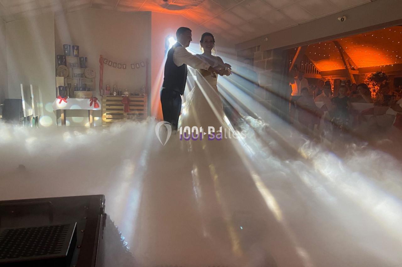 Un couple danse dans une salle éclairée par des faisceaux lumineux, entouré d'une ambiance de fumée.