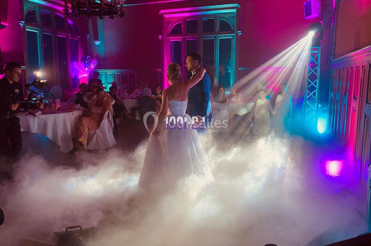 Un couple danse au milieu d'une salle éclairée par des lumières colorées et entourée d'une fumée légère.