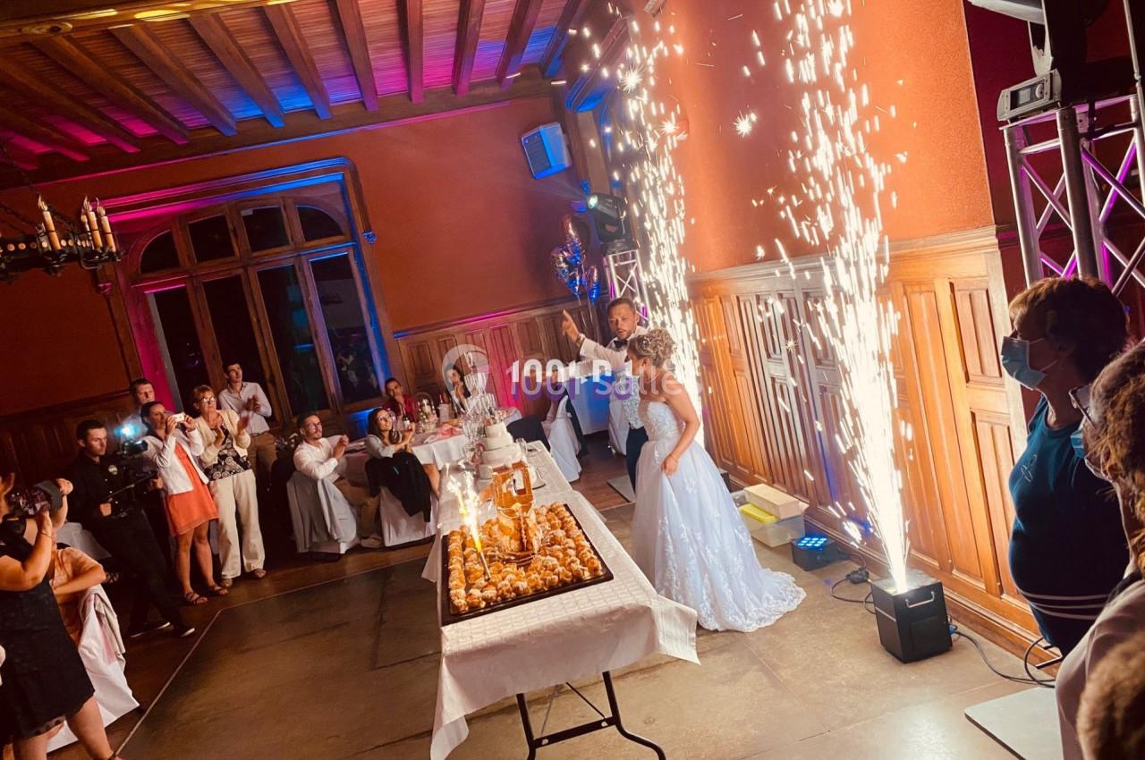 Un couple de mariés coupe leur pièce montée dans une salle festive avec des étincelles en arrière-plan.