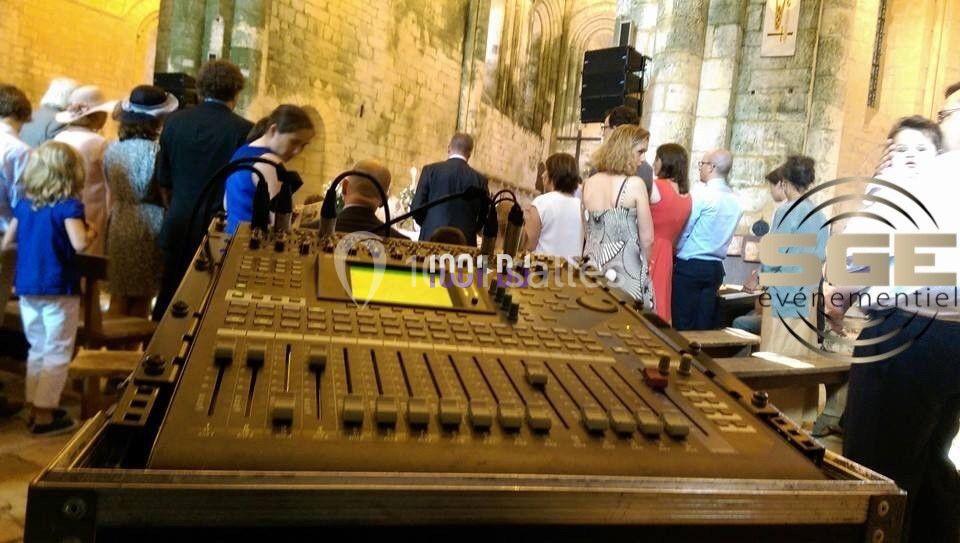 Table de mixage audio en premier plan dans une église, avec des personnes rassemblées en arrière-plan.