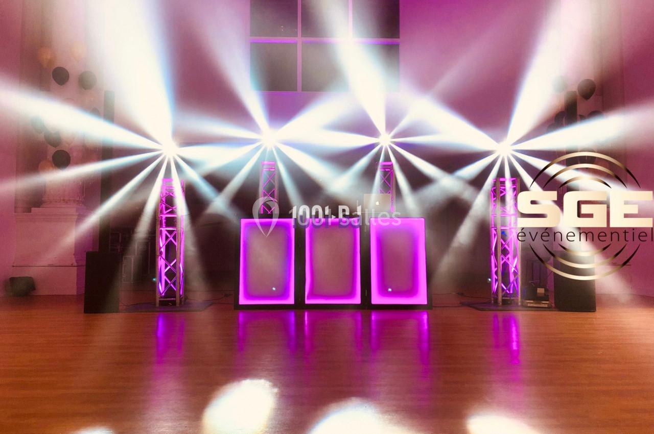 Installation lumineuse avec projecteurs LED colorés et panneaux lumineux violets dans une salle d'événement.