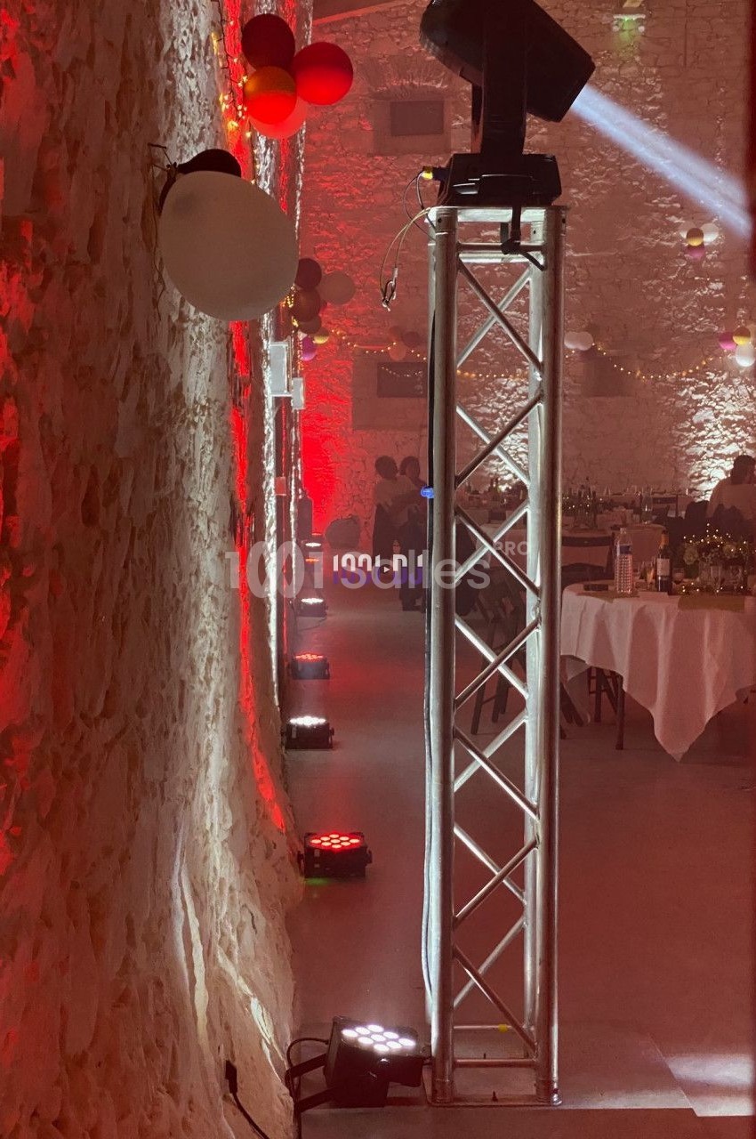 Salle en pierre éclairée de lumières rouges et blanches, avec des tables dressées et des équipements d'éclairage.