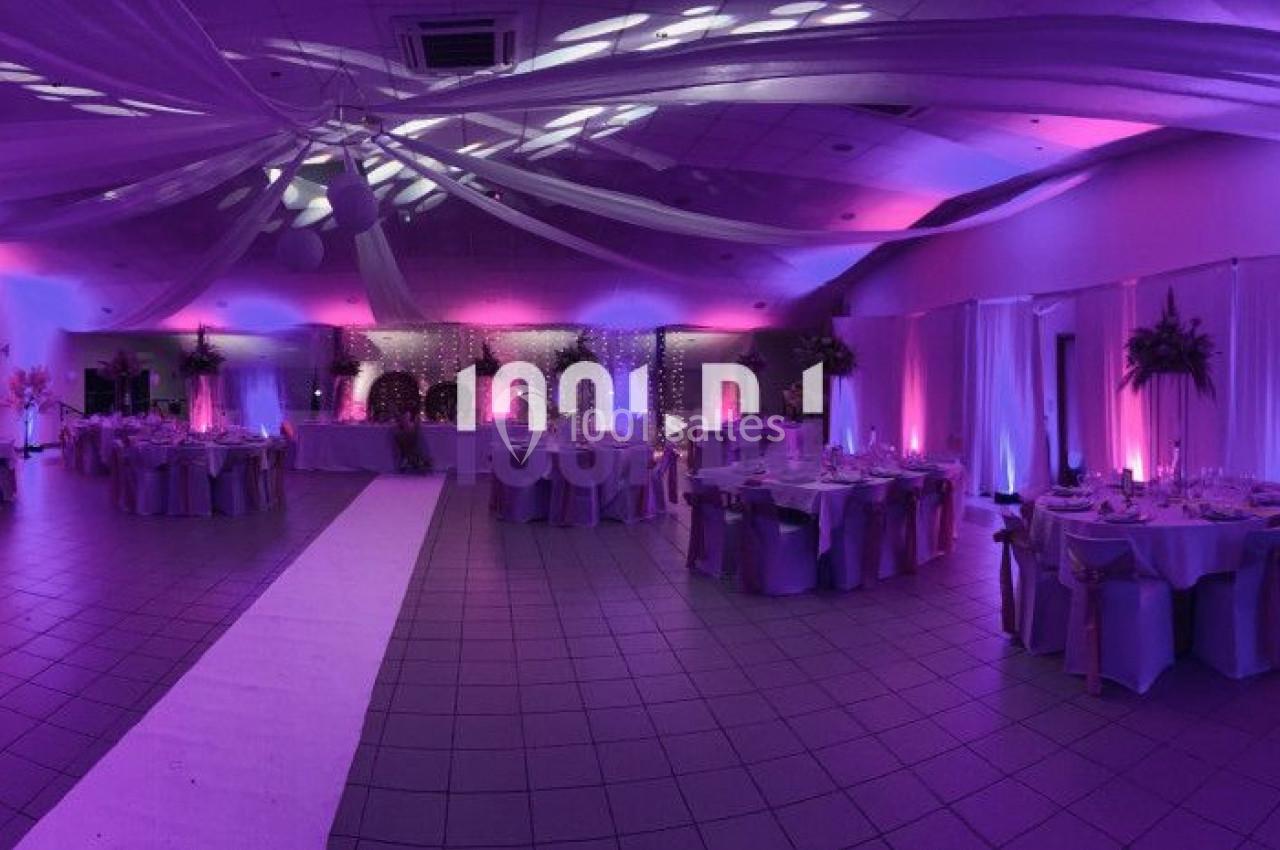 Salle de réception décorée avec des lumières violettes, tables dressées et plafond orné de voilages blancs.