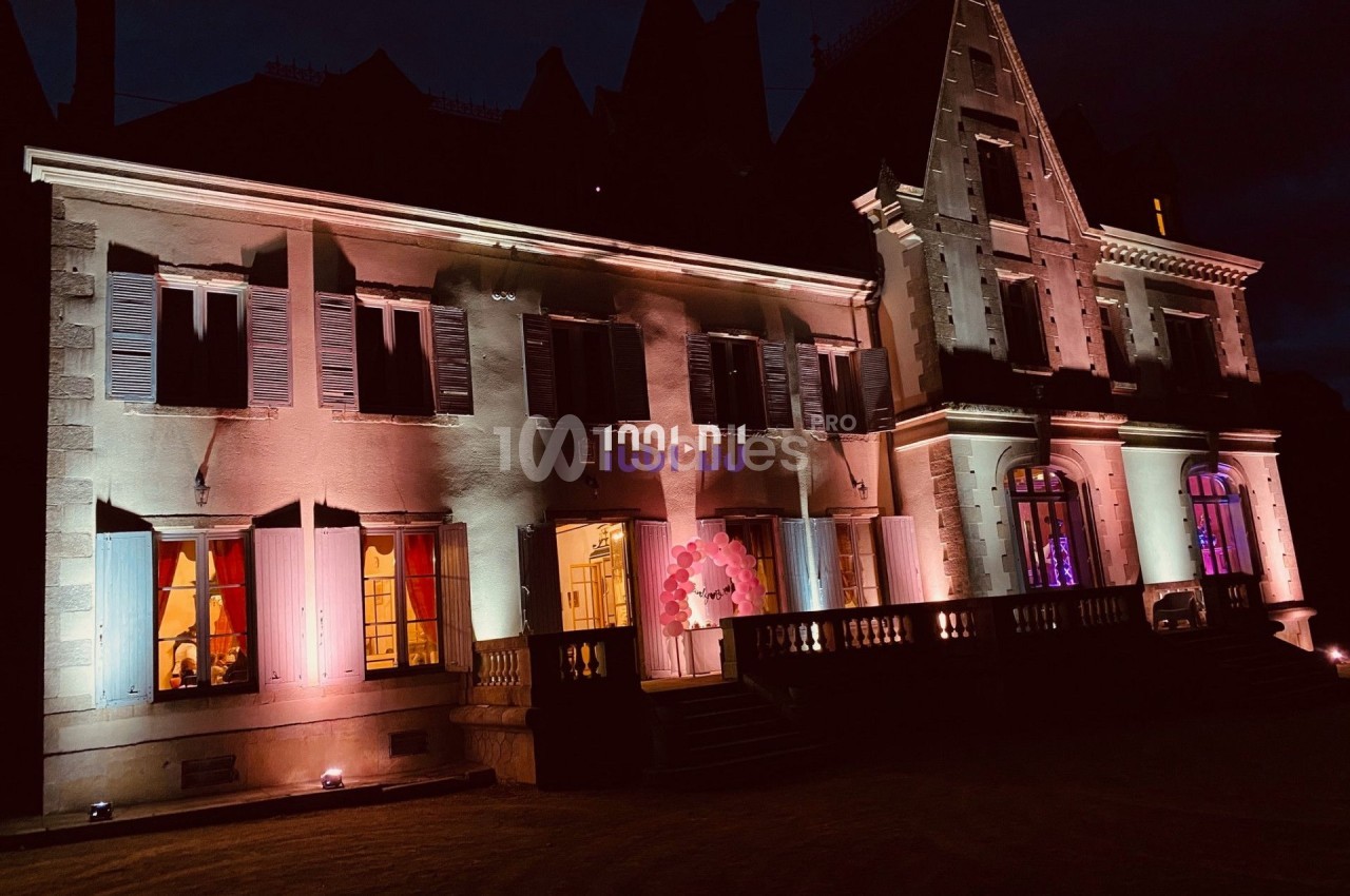Façade d'un bâtiment ancien éclairé par des lumières colorées dans une ambiance nocturne.