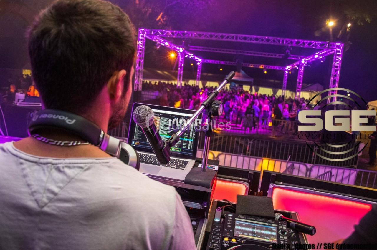 Un DJ mixe sur scène lors d'un événement nocturne avec une foule et des lumières violettes en arrière-plan.