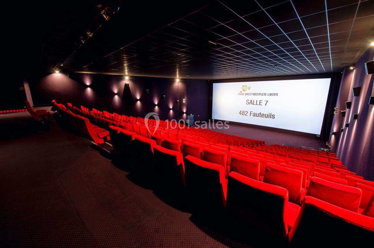 Salle de cinéma vide avec des rangées de fauteuils rouges et un écran affichant ’Salle 7, 482 fauteuils’.