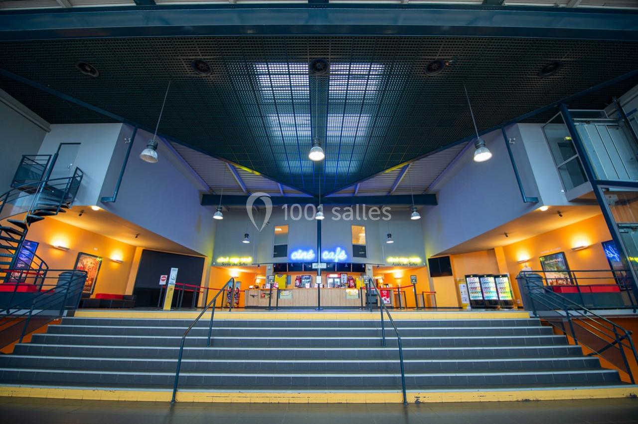 Vue intérieure d'un hall de cinéma avec un comptoir de confiserie éclairé et des escaliers au premier plan.