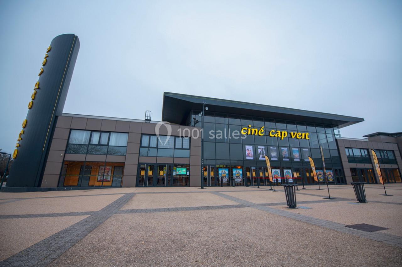 Façade moderne d'un cinéma avec enseigne ’Ciné Cap Vert’, grandes baies vitrées et esplanade dégagée au premier plan.