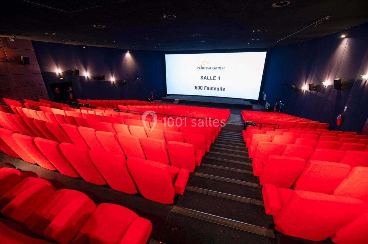 Salle de cinéma vide avec des rangées de fauteuils rouges et un écran blanc affichant ’Salle 1 - 600 fauteuils’.