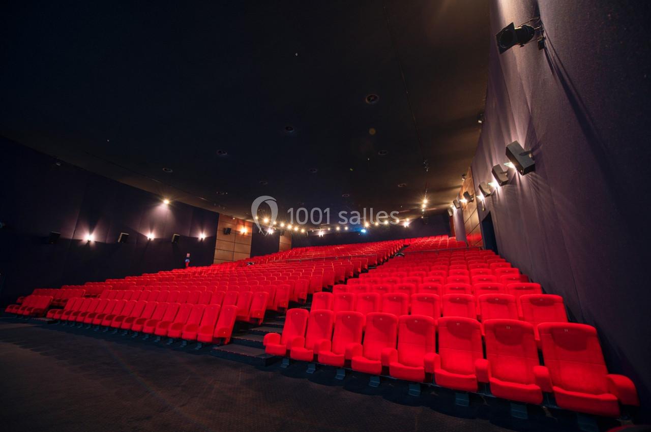 Salle de cinéma vide avec rangées de fauteuils rouges et éclairage tamisé au plafond.
