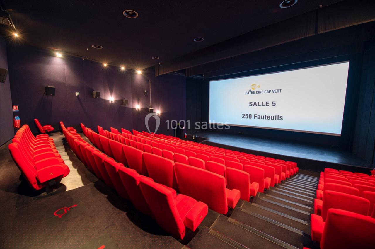 Salle de cinéma avec des rangées de fauteuils rouges vides et un écran affichant des informations sur la salle.