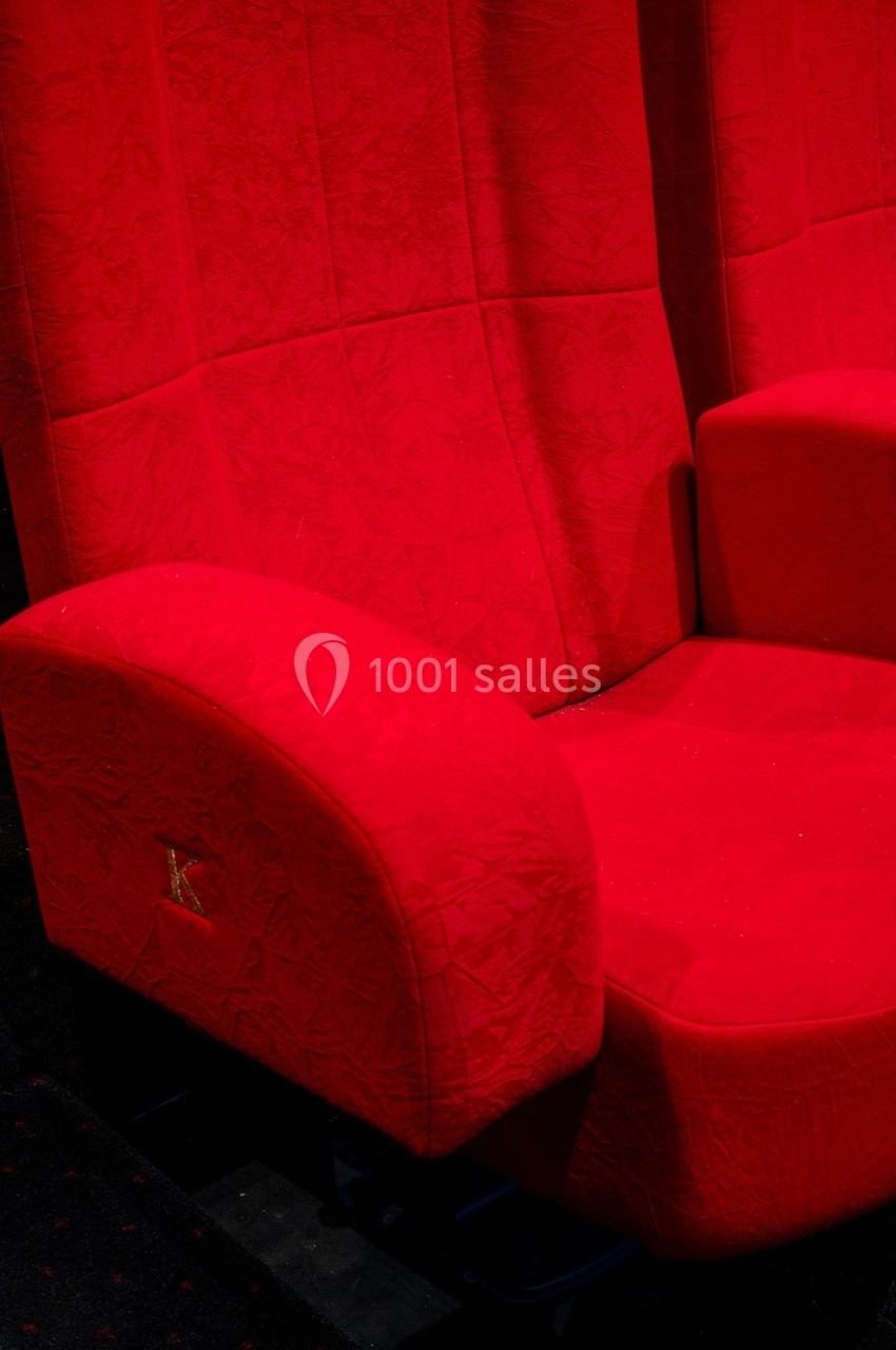 Fauteuil de cinéma rouge avec accoudoirs, placé sur un sol sombre.