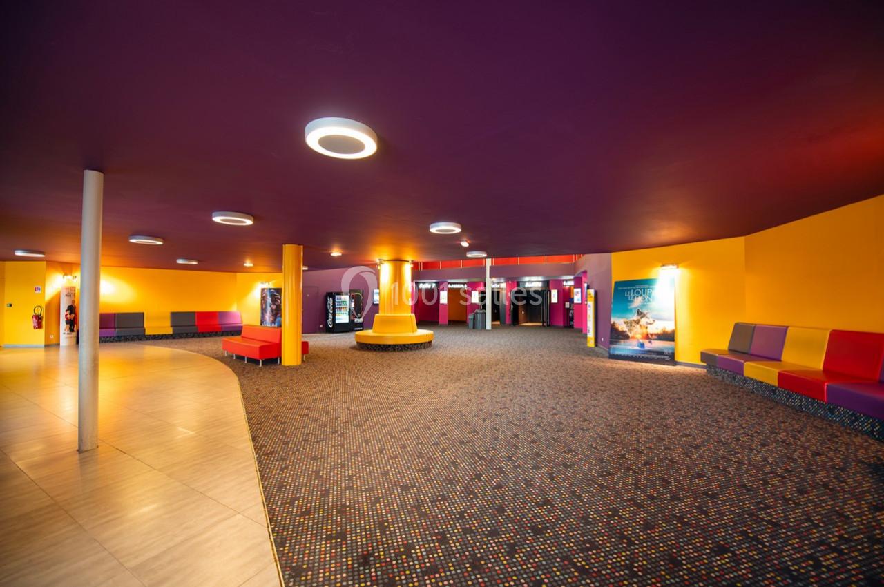 Hall d'entrée spacieux avec moquette colorée, sièges vifs, distributeurs automatiques et affiches de films.