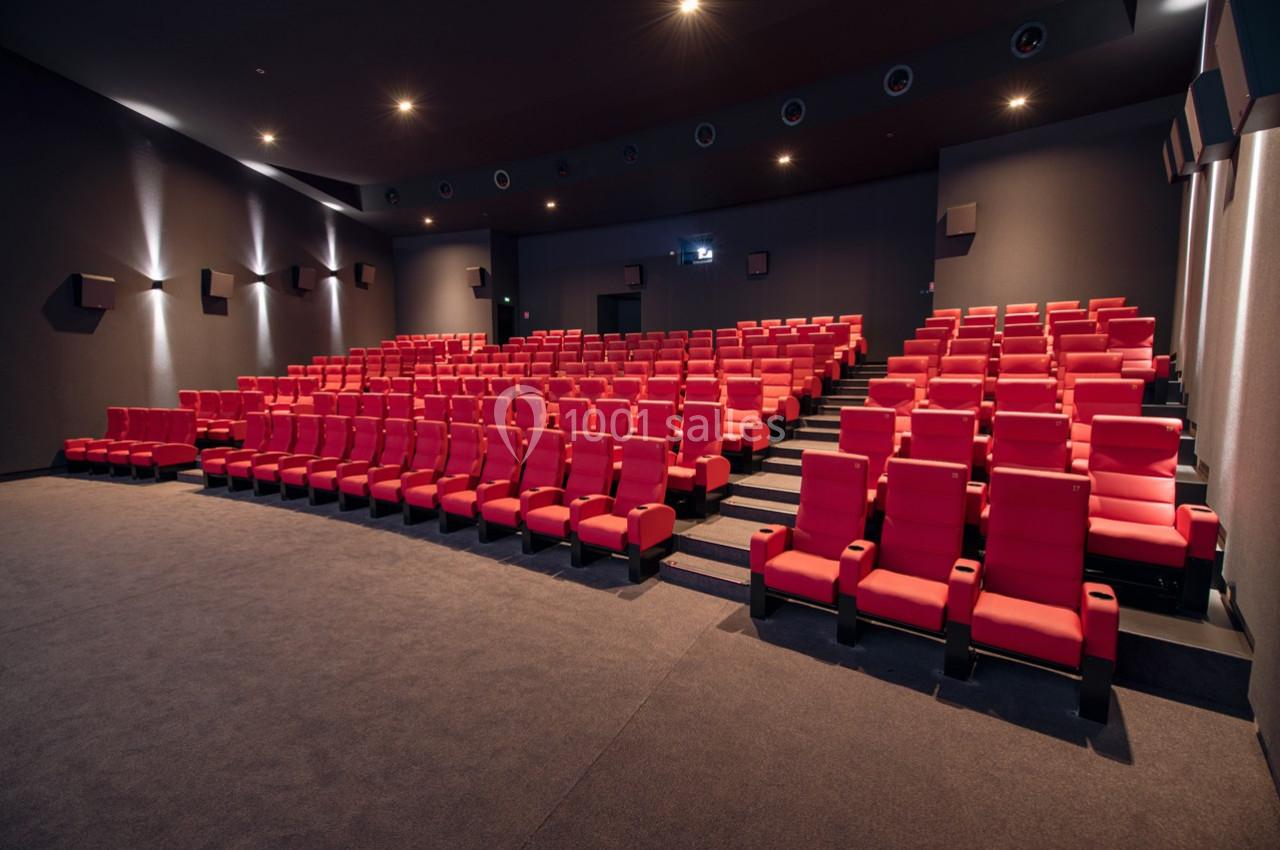 Salle de cinéma vide avec des rangées de fauteuils rouges alignés et un écran blanc en arrière-plan.