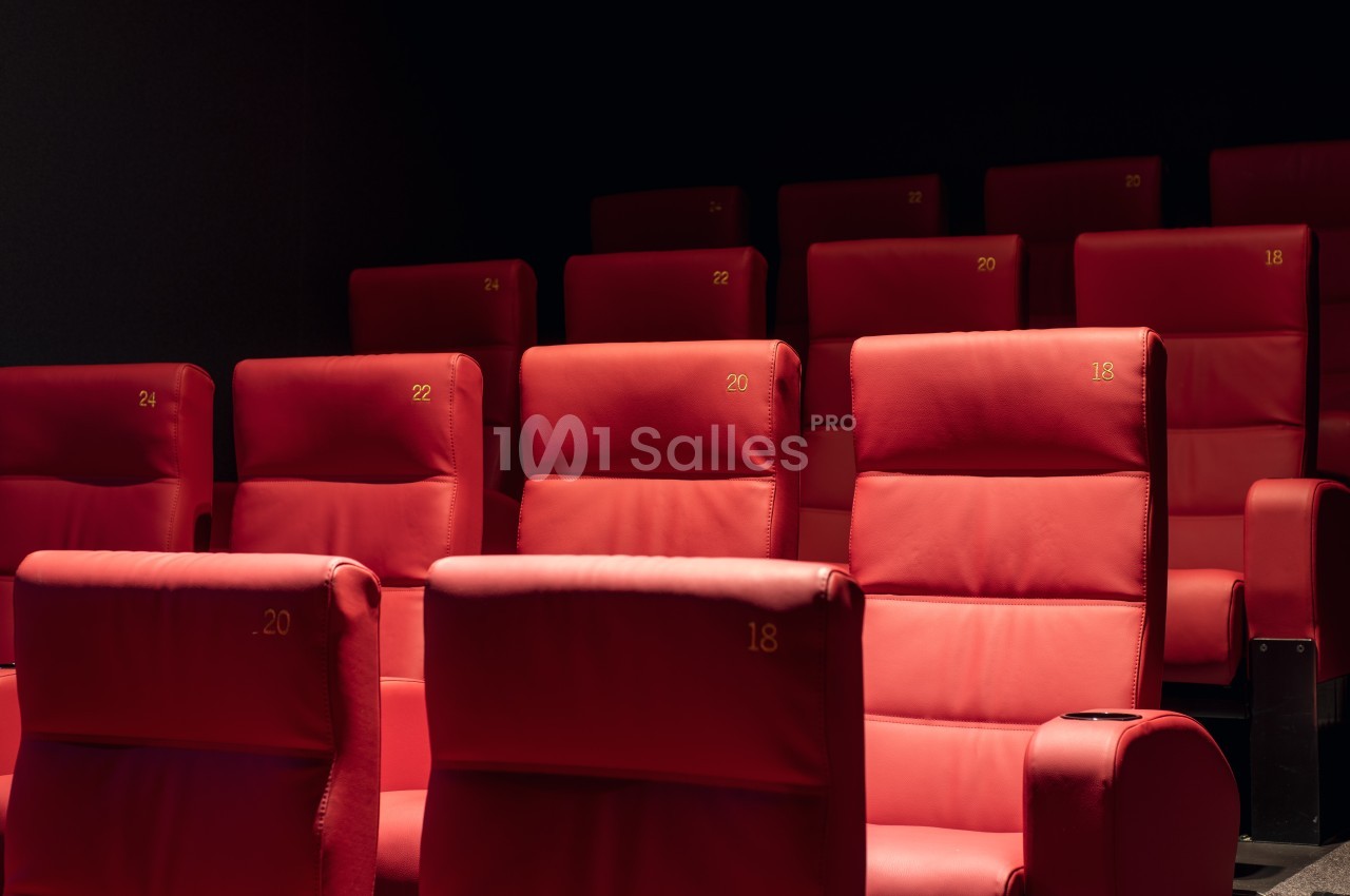 Fauteuils rouges numérotés alignés dans une salle de cinéma sombre.