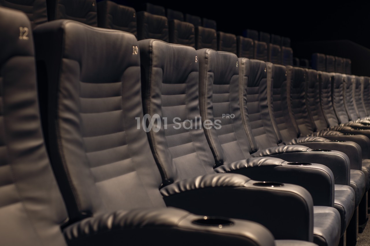 Rangée de fauteuils en cuir noir dans une salle de cinéma vide.