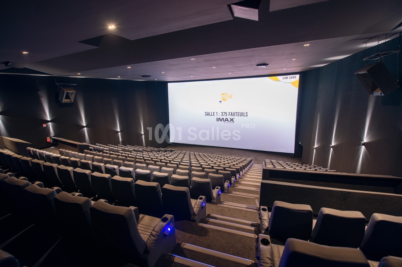 Salle de cinéma moderne avec sièges inclinés, grand écran IMAX et éclairage tamisé.