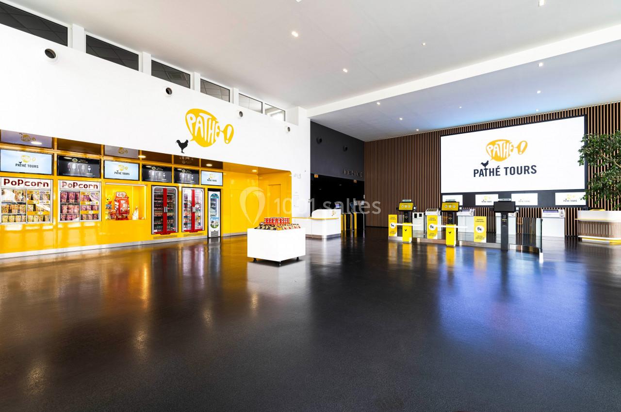 Hall d'entrée lumineux d'un cinéma avec comptoirs, distributeurs de snacks et écran affichant ’Pathé Tours’.