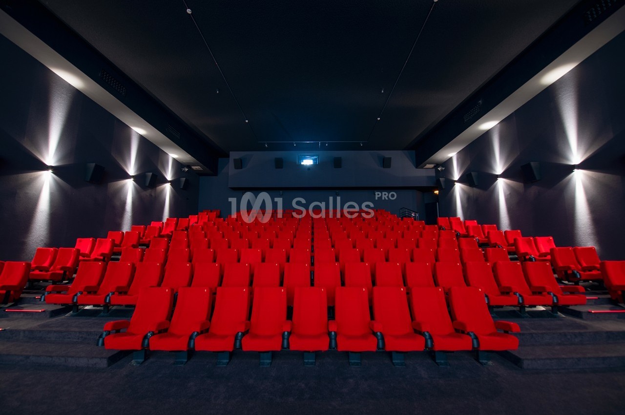 Salle de cinéma vide avec des rangées de sièges rouges et un écran blanc en arrière-plan.
