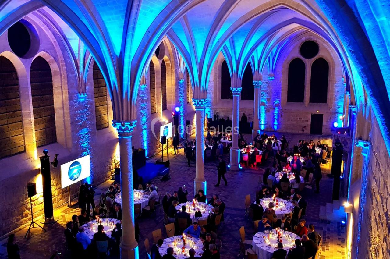Salle voûtée éclairée en bleu accueillant un dîner avec des tables rondes dressées et des convives assis.