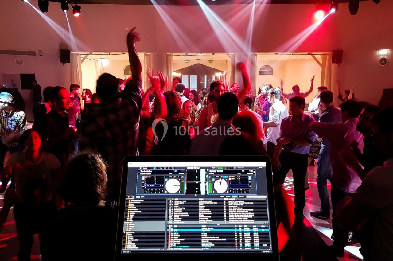 Vue d'une fête avec des personnes dansant sous des lumières colorées, écran de DJ en premier plan.