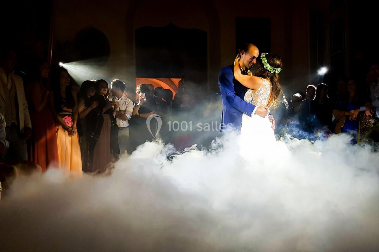 Un couple danse au milieu d'une piste entourée de fumée, sous le regard des invités dans une ambiance tamisée.