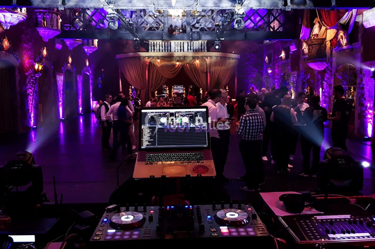 Vue depuis une table de mixage avec ordinateur, éclairages colorés et invités dansant dans une salle de réception.