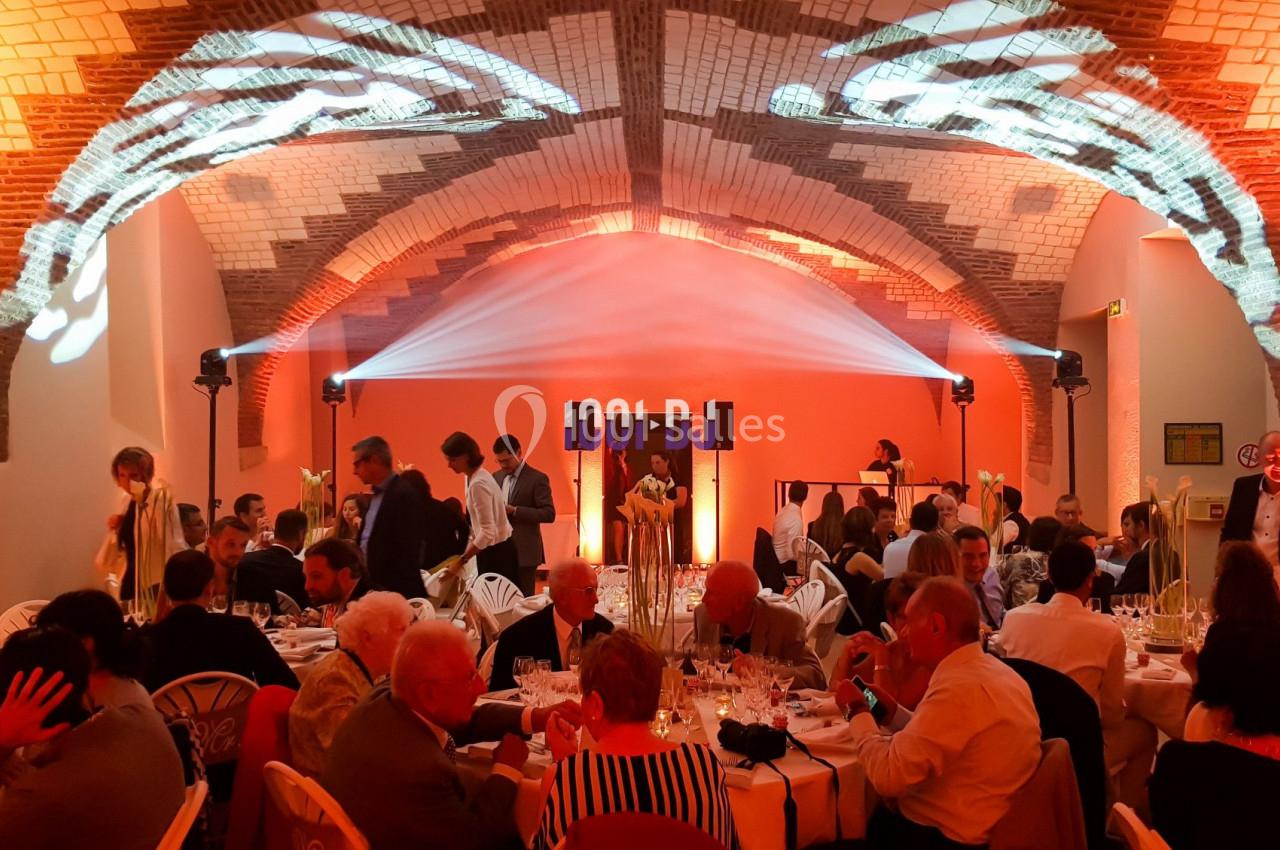 Salle voûtée illuminée en orange, avec des invités assis à des tables rondes lors d'un événement festif.