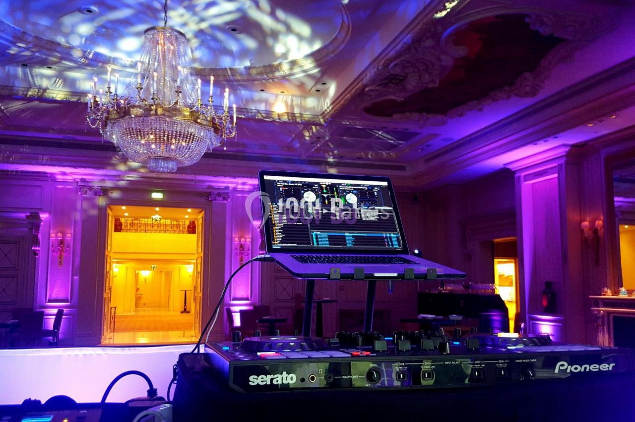 Console de DJ avec ordinateur portable dans une salle élégante éclairée par des lumières colorées et un grand lustre.