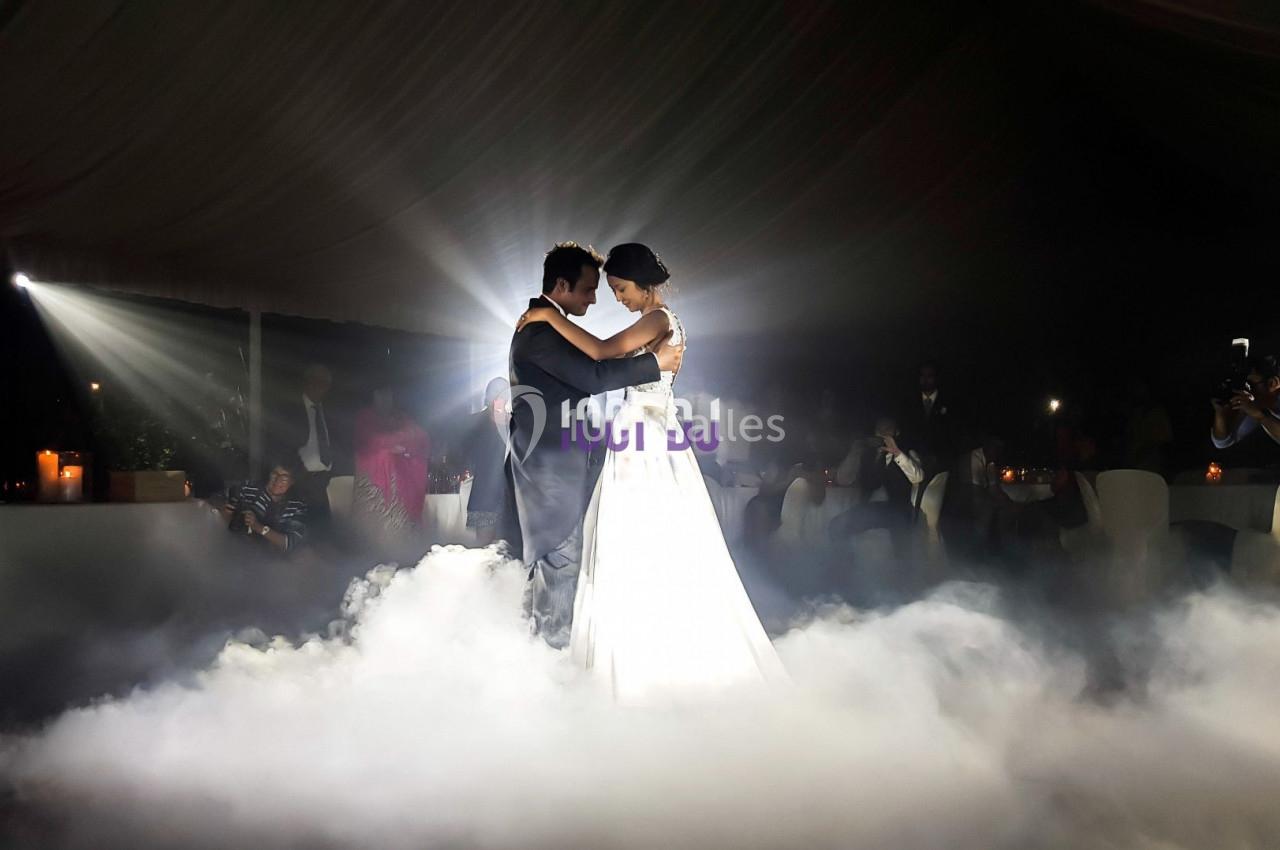 Un couple danse dans une salle sombre éclairée par des projecteurs, entouré de fumée au sol.