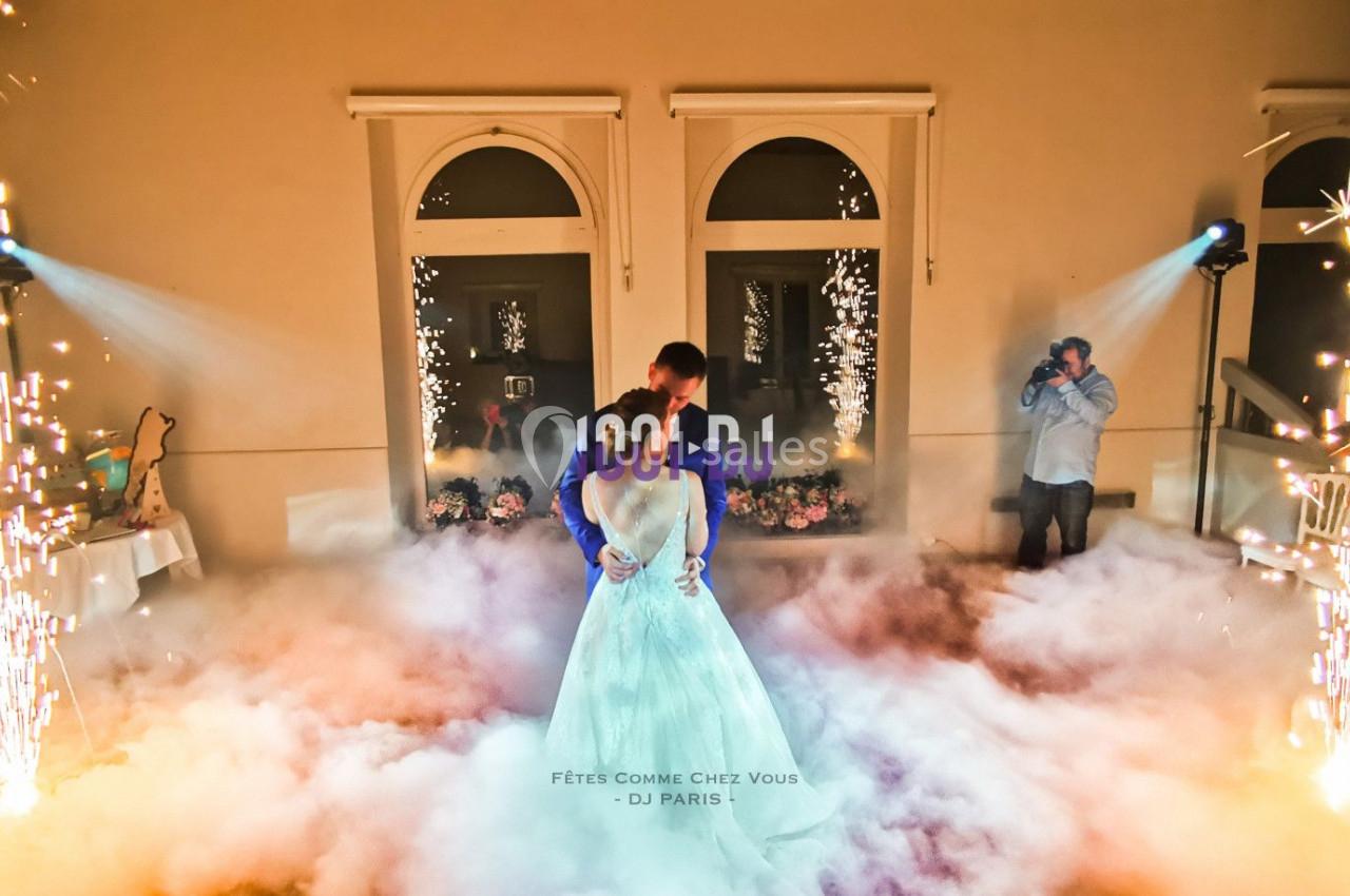 Un couple danse au milieu d'une piste entourée de fumée et d'effets pyrotechniques dans une salle éclairée.