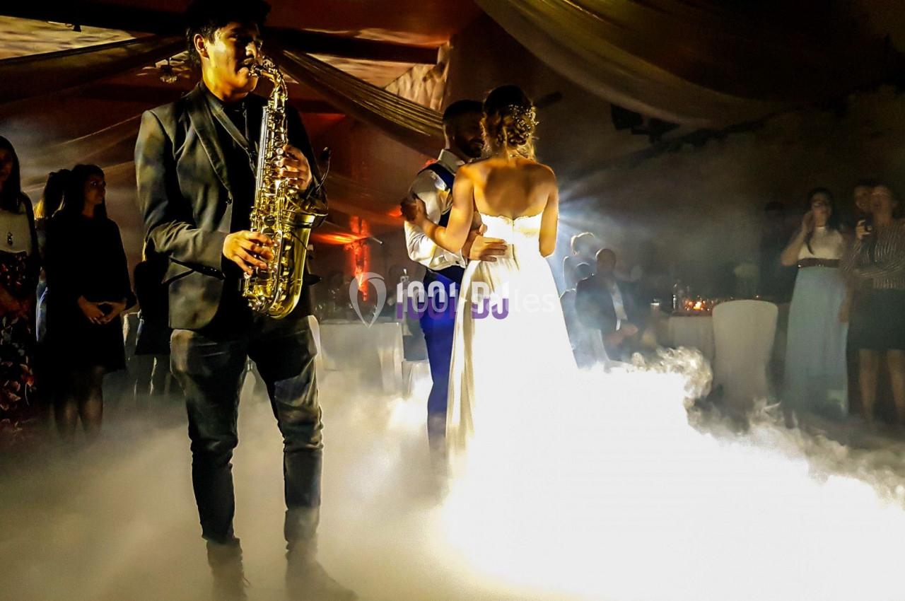 Un couple danse au milieu d'une piste entourée de fumée, tandis qu'un musicien joue du saxophone en avant-plan.